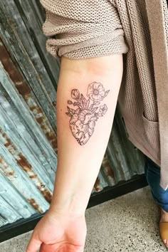 a woman's arm with a tattoo on it that has flowers in the shape of a heart