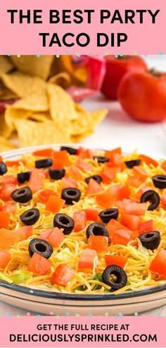 the best party taco dip recipe with black olives, tomatoes and cheese on top