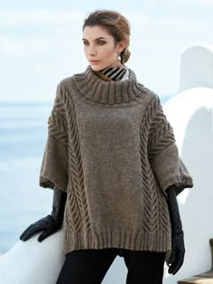 a woman standing next to the ocean wearing a sweater and gloves