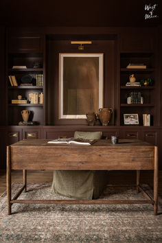 a wooden desk sitting in the middle of a living room next to a book shelf