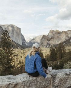 a woman sitting on top of a large rock next to a forest filled with trees