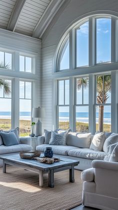 a living room filled with white furniture and large windows overlooking the ocean on a sunny day