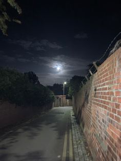 the moon is shining brightly in the night sky over a brick wall and fenced street