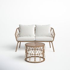 a wicker couch and coffee table with white pillows on it in front of a plain background