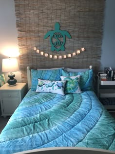 a bed with blue sheets and pillows in front of a sea turtle wall hanging above it