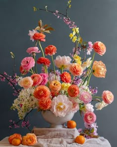 a white vase filled with lots of colorful flowers on top of a table next to an orange slice