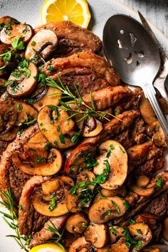 a white plate topped with meat and mushrooms next to lemon wedges on top of a wooden table