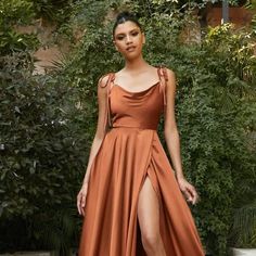 a woman in an orange dress standing next to some bushes and trees with her legs high