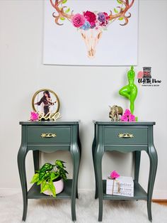 two green nightstands with flowers on them in front of a deer skull mounted to the wall