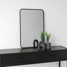 a black table with a mirror and some plants sitting on it's sideboard