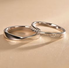 two white gold wedding rings with diamonds on them sitting on a beige surface in the sunlight