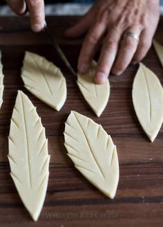 a person cutting up leaves with a knife on a wooden table in front of them