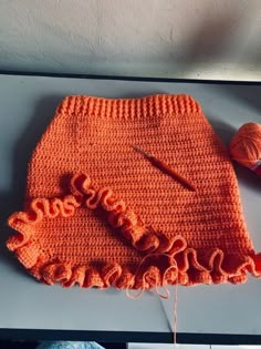 an orange crochet skirt with yarn and scissors on the table next to it