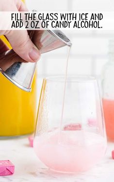 a person pouring pink liquid into a glass with ice and candy in front of them