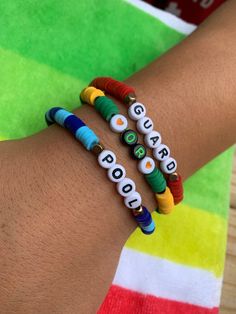 two bracelets with words on them sitting on a person's arm in front of a colorful towel