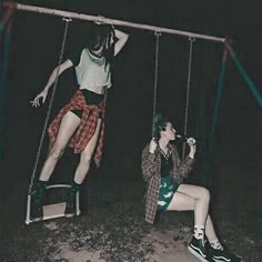 two people are sitting on swings in the dark, one is holding onto another person's leg