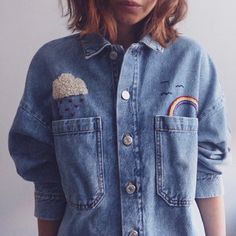 a woman wearing a denim jacket with patches and rainbows on the front, she has her hands in her pockets