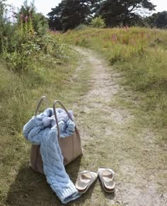 a handbag and pair of slippers sitting on the side of a dirt road