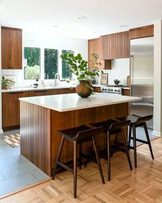 a kitchen with wooden cabinets and white counter tops, along with two stools that match the hardwood flooring