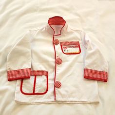 a white jacket with red trims and patches on the chest, sitting on a bed