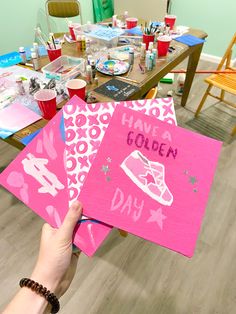 a person holding up some pink paper on top of a table with other crafting supplies