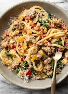 a bowl full of pasta with meat, spinach and cheese on it next to a fork