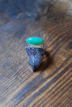 This ring is decorated with an alluring combination of all natural vivid and glowing gems. A striking bright green bubbly Australian chrysoprase glows while sitting beside a rich in color crystalized Petrified Wood, stark and playful in pattern.  One of a kind for their amazing organic palette and patterns. Ring is entirely hand formed, forged and built from raw sterling sheet. Curved to cradle your finger and tapered at the back for a comfortable fit. Fits like a standard ring.  Fits size 10. Green Turquoise Ring With Natural Stones, Green Emerald Fusion Ring, Green Oval Fusion Rings, Green Emerald Fusion Style Ring, Green Chrysocolla Rings With Natural Stones, Green Chrysocolla Gemstone Ring, Unique Turquoise Multi-stone Opal Ring, Oval Green Chrysocolla Rings, Unique Green Turquoise Ring With Large Stone