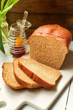 sliced loaf of bread sitting on top of a cutting board next to honey and flowers