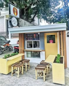 the outside of a small restaurant with benches and tables in front of it, next to a tree