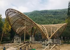 a bamboo structure is being constructed in front of a mountain side area with trees and mountains behind it