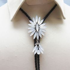 a woman wearing a white shirt and black string necklace with silver flowers on the front