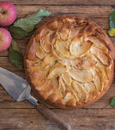 an apple pie on a wooden table with apples around it and a knife next to it