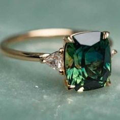 an emerald colored ring with three diamonds on it's sides, sitting on a green surface