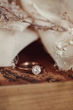 an engagement ring sitting on top of a wooden box next to white flowers and branches