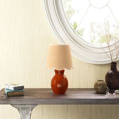 an orange vase sitting on top of a table next to a lamp