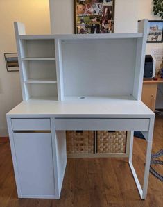 a white desk with shelves and baskets on the bottom shelf, in front of a wooden floor