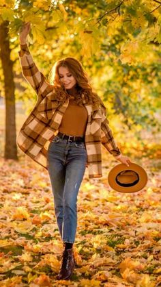 a beautiful young woman walking through the leaves in an autumn park with her hat up