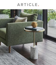 a green couch sitting next to a table on top of a wooden floor in front of a window