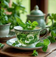 a glass cup filled with green leaves on top of a wooden table