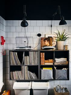 a shelf filled with lots of records next to a wall mounted lamp and two hanging lights