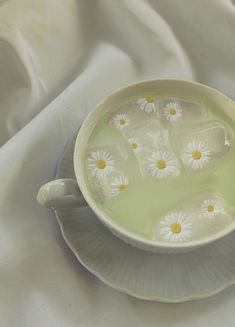 a cup filled with water and daisies sitting on top of a saucer next to a white cloth