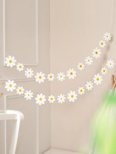 a woman is hanging daisies on a string in a room with a chair and table