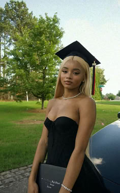 a young woman wearing a graduation gown and holding a book in front of a car