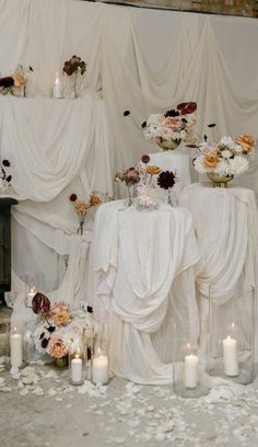 the table is covered with white cloths and decorated with flowers, candles and votives