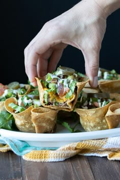 a hand picking up a tortilla filled with guacamole and lettuce