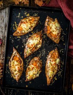 baked sweet potatoes with cheese and herbs on a baking sheet, surrounded by autumn leaves