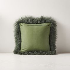 a green pillow with grey fur on the bottom and side, against a white wall