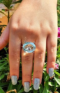 a woman's hand with blue and silver nail polish holding an oval shaped ring