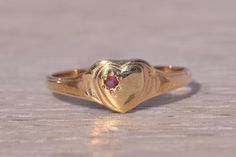 This stunning piece, known as The Heartfelt Ruby, features a captivating natural ruby set at the center of a heart motif. The natural ruby adds a touch of color and elegance, making it a delightful piece for any collection. The ring is crafted in yellow gold and is currently a finger size 4 but can be adjusted to any finger size for an additional charge upon request, ensuring a perfect fit. Love this piece, but don't have the money to spend right now? We offer FREE layaway on every item in our shop. With just 20% down, take one full year (interest-free) to pay off your new jewelry! There are no hidden fees or charges, ever. For more information on our layaway policy, please contact us. Each piece has been hand-selected and meticulously identified and graded by a Graduate Gemologist who has Fine Ruby Heart-shaped Jewelry, Fine Ruby Heart Jewelry, Dainty Heart Shaped Solitaire Jewelry, Ruby Heart Charm Jewelry, Dainty Heart Solitaire Jewelry, Ruby Birthstone Heart Ring, Ruby Heart Ring With Birthstone, Heart-shaped Ruby Ring For Wedding, Anniversary Yellow Gold Ruby Ring With Heart Shape