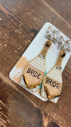 the bride and groom earrings are sitting on top of a wooden table with gold accents